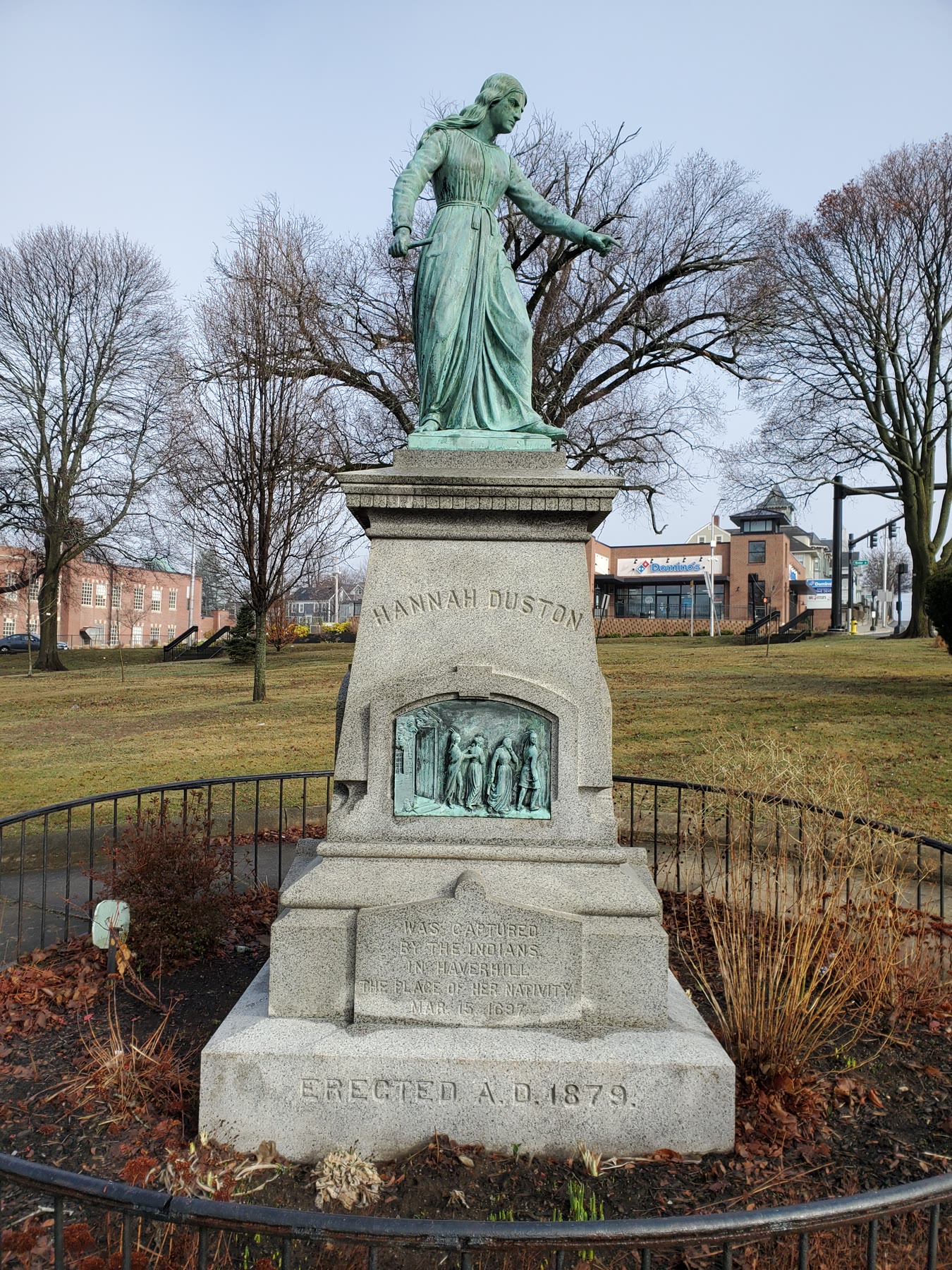 The 1879 bronze of Hannah Duston in Haverhill, a green figure with a hatchet on a granite base in a park, photographed in 2022.